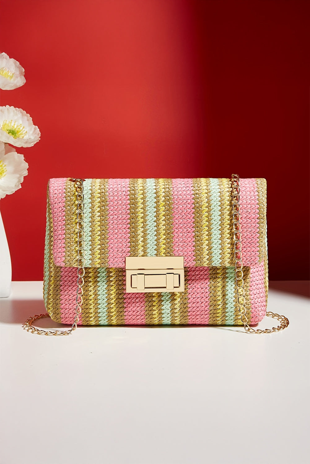 Striped handbag with a gold chain on a white surface against a red background