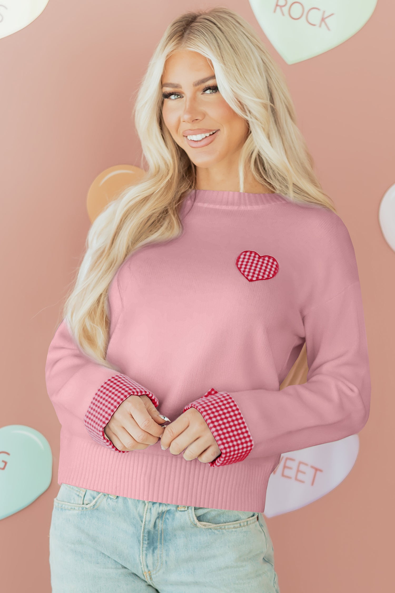 Woman wearing a pink sweater with a heart design in front of a pink background with heart shapes.