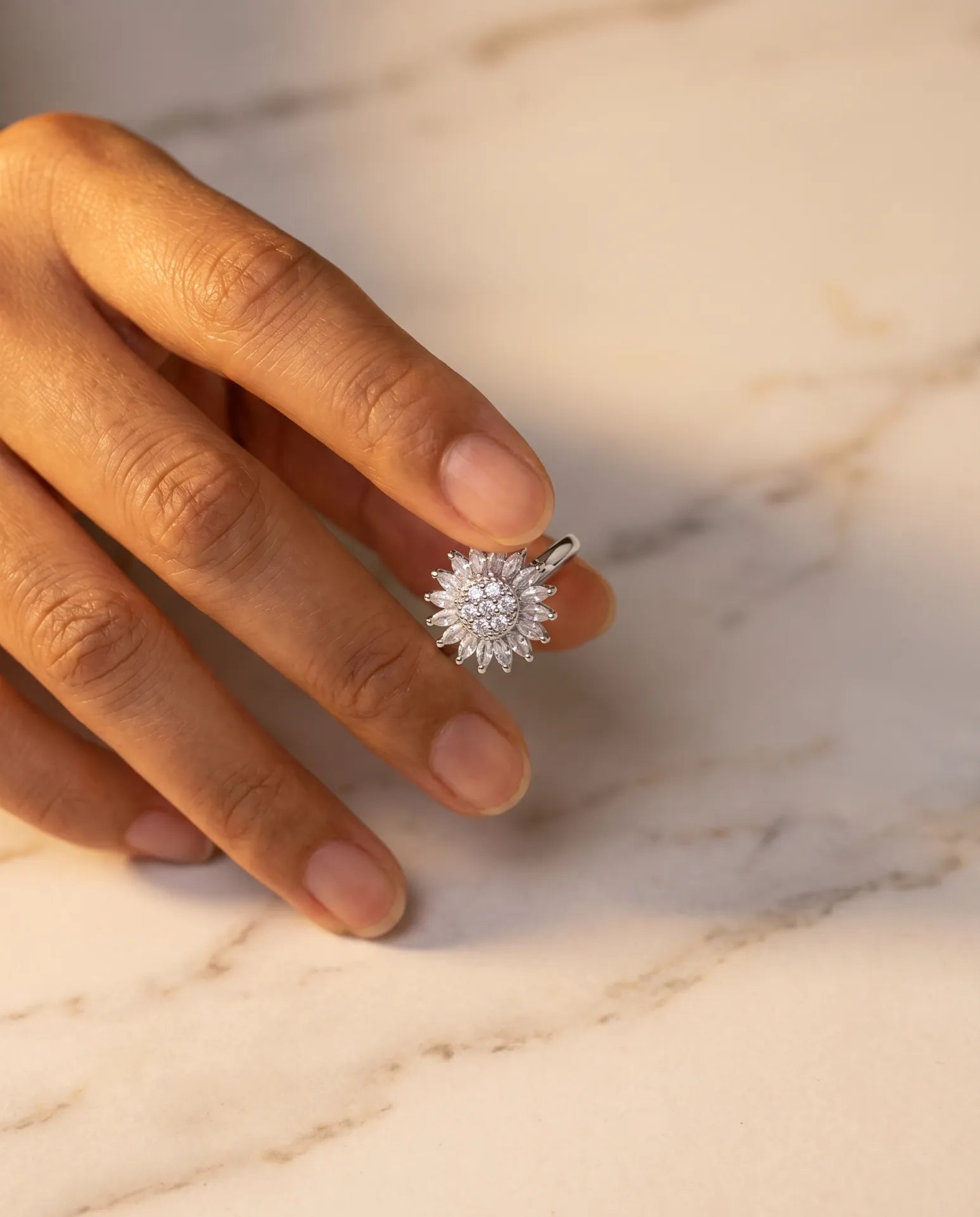 Sunflower Rotation Ring in silver — worn on hand, sunflower detail on warm marble surface