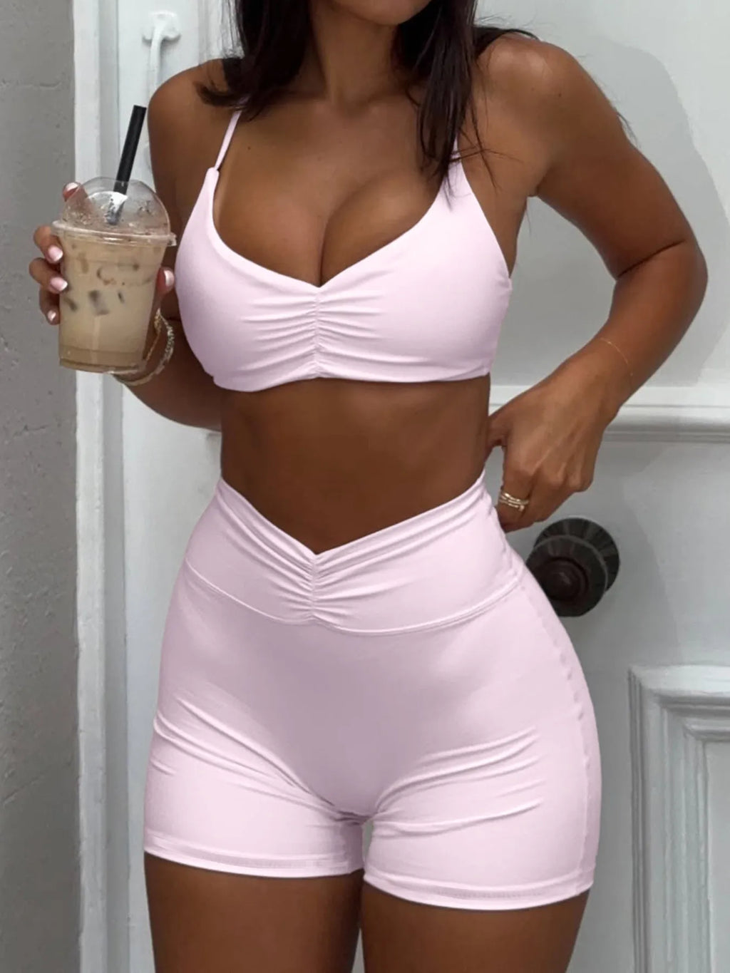 Model wearing a pink sports bra and shorts set, holding an iced coffee- DEA Collection 