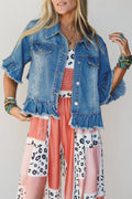 A woman wearing a light blue denim jacket with ruffled sleeves and hem, layered over a white top with pink and red patterned fabric, paired with pink patchwork wide-leg pants with black animal prints.